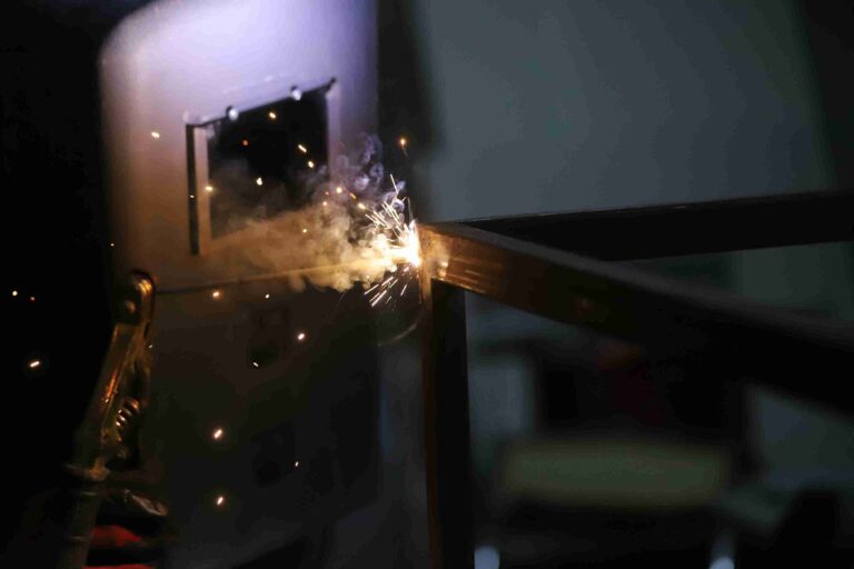 Welding sparks fly from a metal joint in a dim workshop scene.