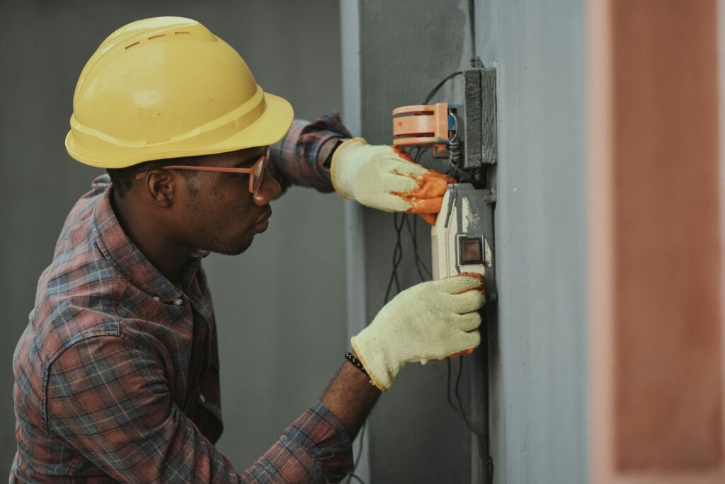 Electrician in a hard hat and gloves working on electrical equipment