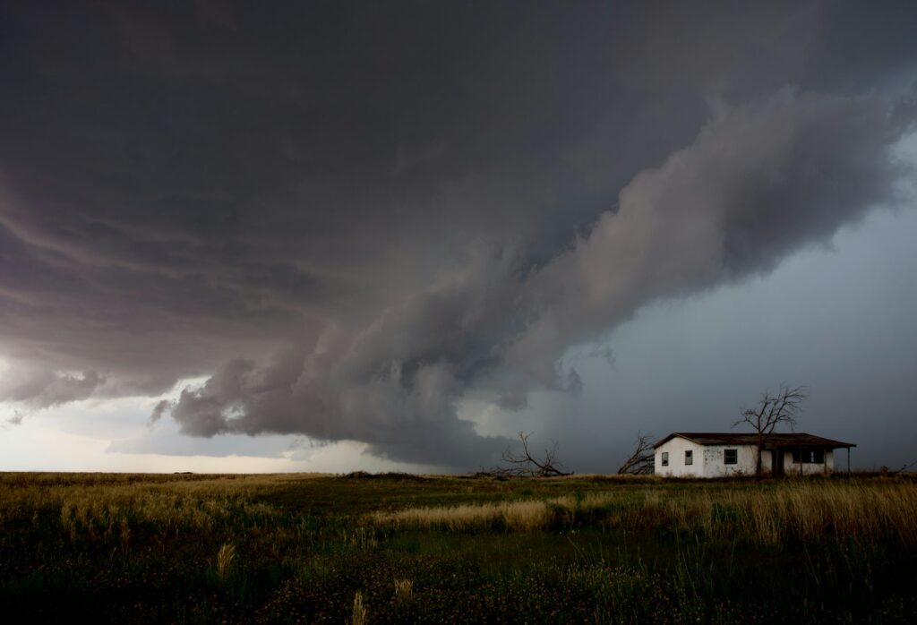 Large storm cloud moving over open farmland and a small house