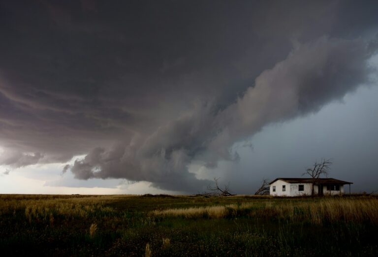 Large storm cloud moving over open farmland and a small house