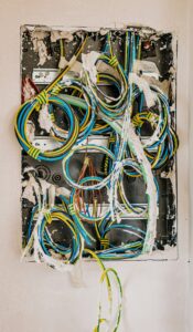 Tangle of electrical wires - Electrician Abilene Open electrical panel with tangled, color-coded cables (blue, yellow, green) spilling out of the box, taped and torn insulation visible.