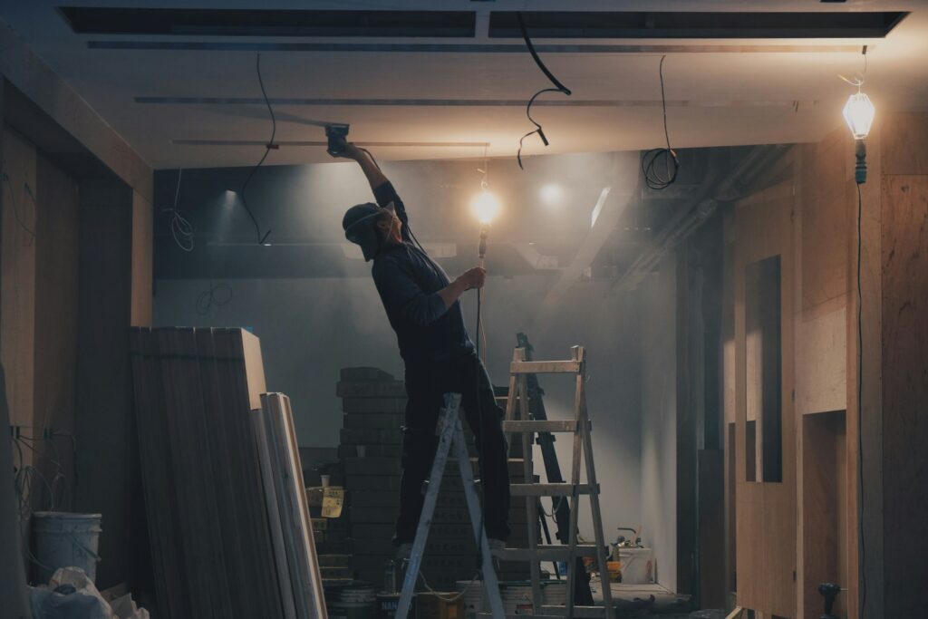 Worker on a ladder running ceiling wiring in an unfinished room